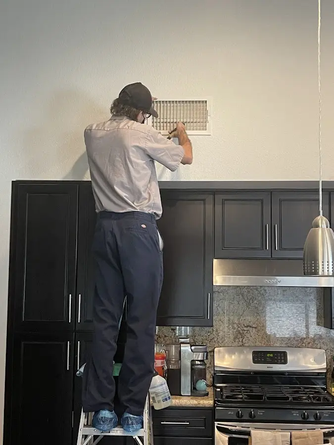 Technician inspecting an air vent during HVAC service in Ada